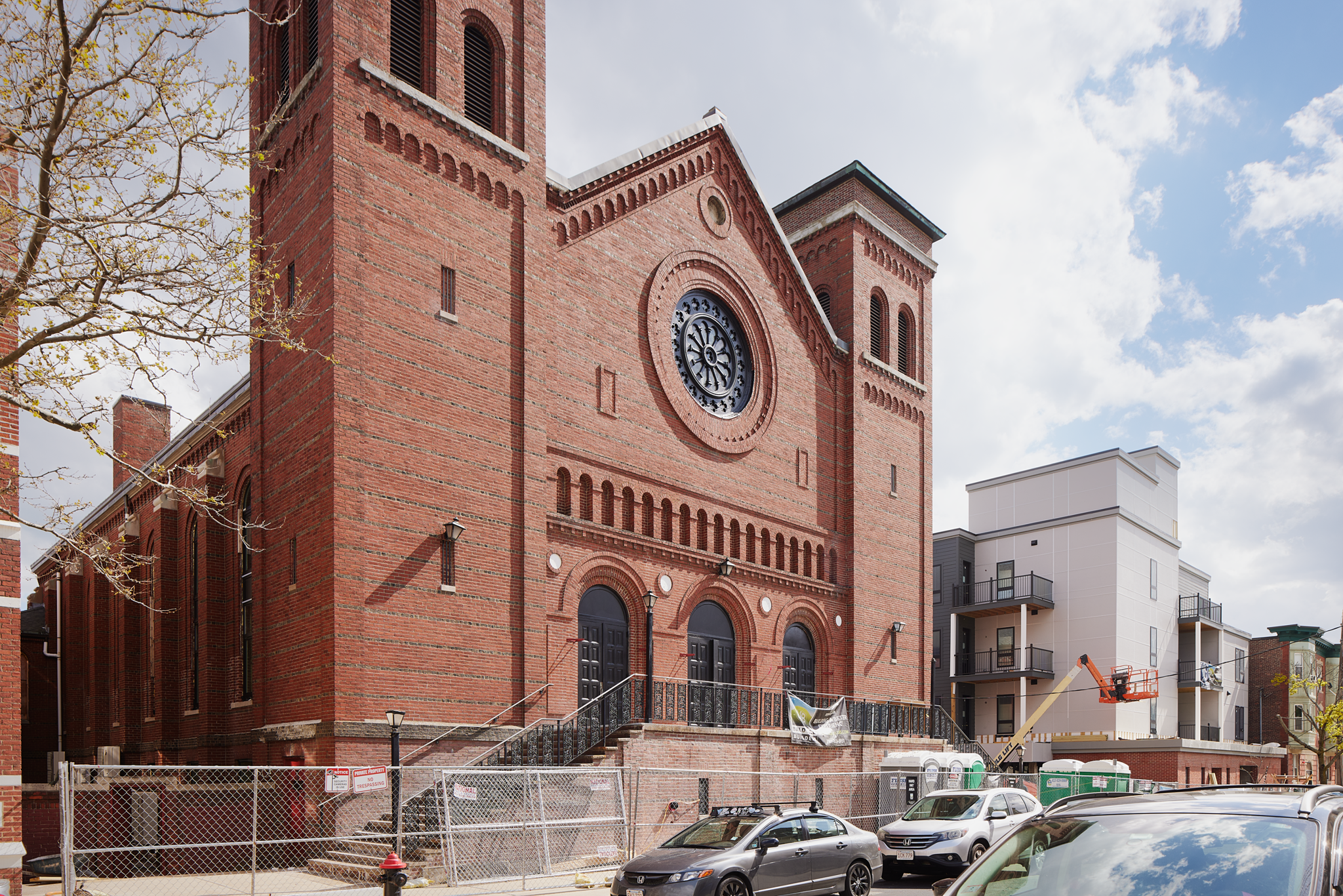 Brick church with rose window and towers behind construction fencing at 163 Chestnut Street in Chelsea, Massachusetts